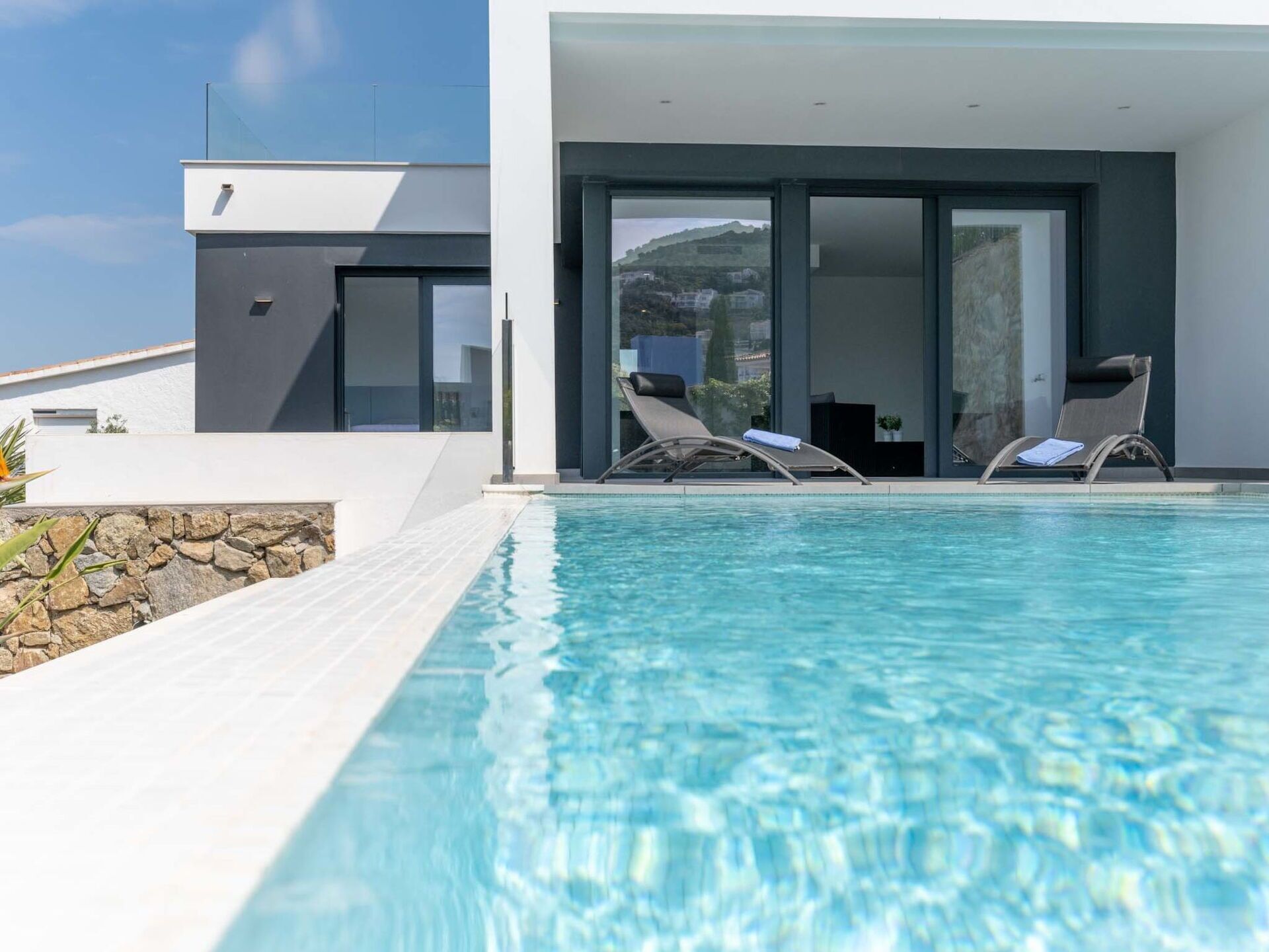 Ein moderner Poolbereich mit zwei Liegestühlen, einer Steinwand und freiem Blick auf die umliegende Landschaft.