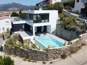 Uma casa moderna de dois andares com piscina, paredes de pedra e vista para as montanhas.