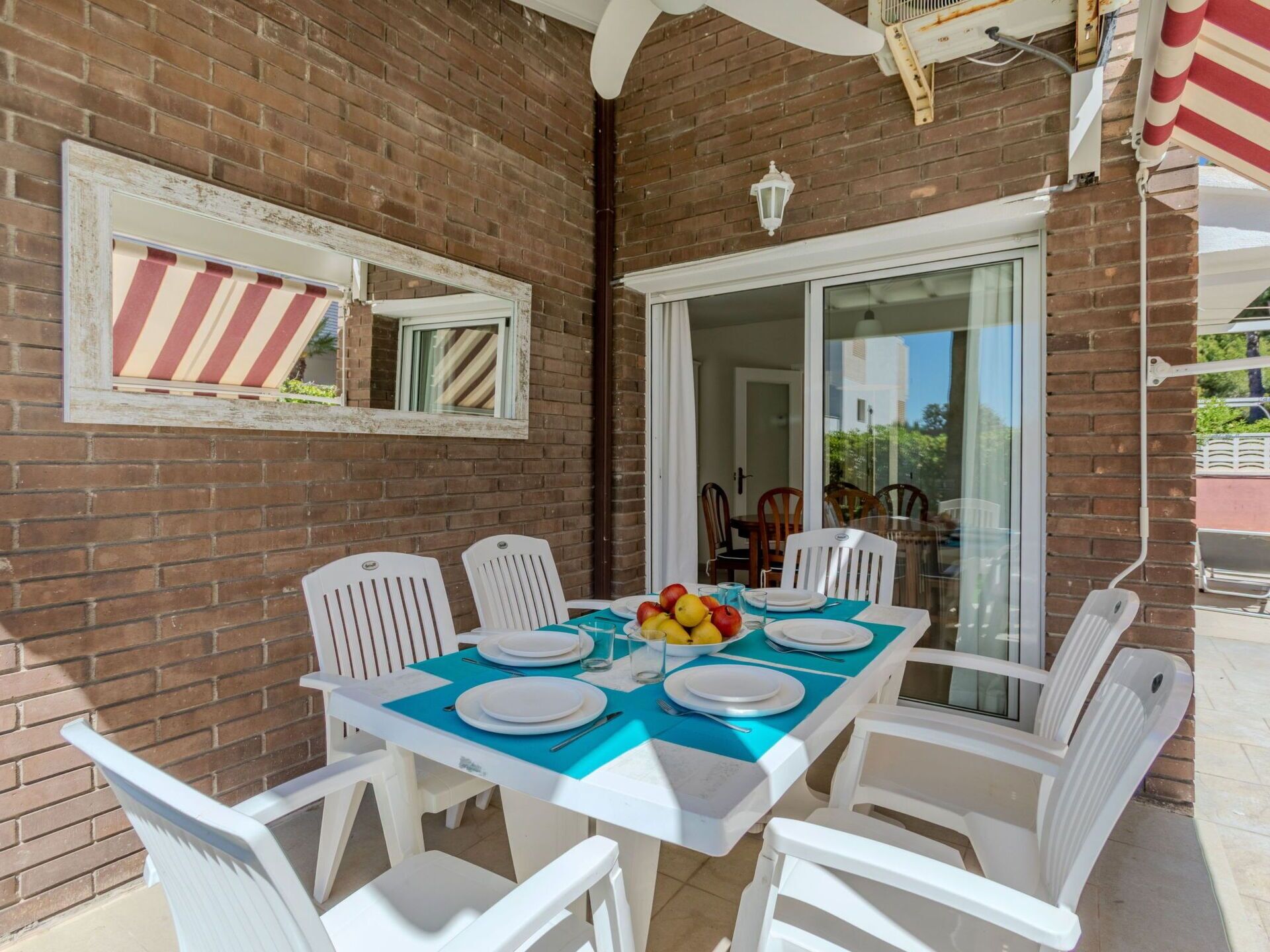 A patio with a table set for four, white chairs, a blue tablecloth, and a fruit bowl.