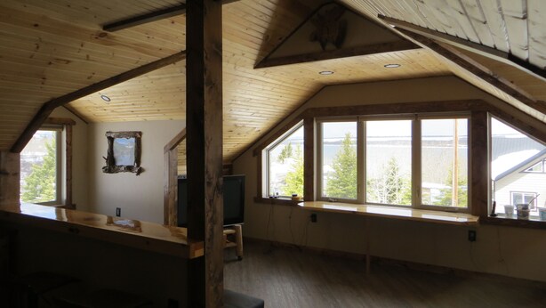 Une pièce spacieuse avec un plafond en pente, de grandes fenêtres donnant sur des arbres et un plan d’eau, et un banc en bois.