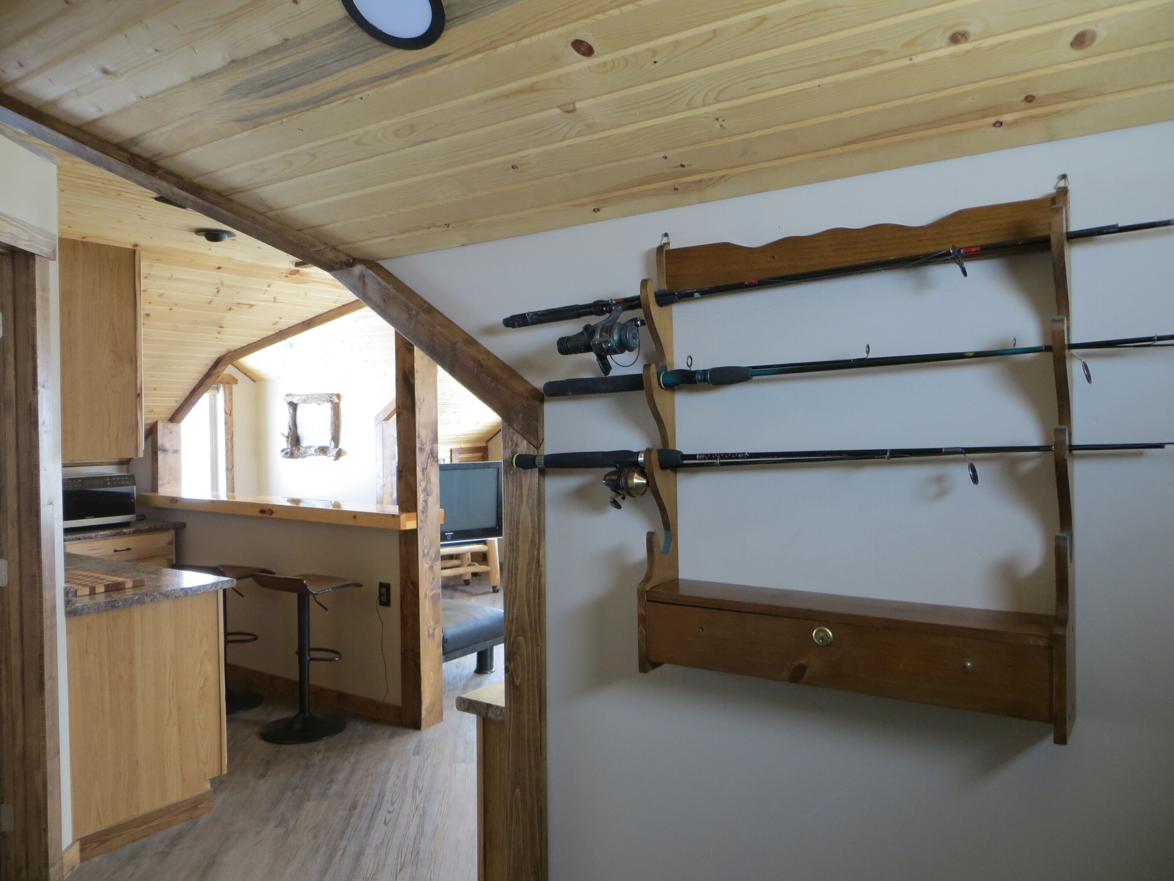A wooden interior with a kitchen area, a bar, and a wall-mounted fishing rod rack.