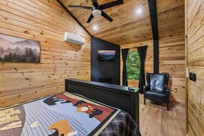 Une chambre dans une cabane en bois, avec un lit, une chaise, une cheminée et un ventilateur de plafond.
