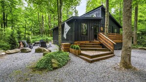 A cabin with a wooden deck, surrounded by trees and gravel. - Romantic Smoky Mountain Getaway • Blackbear Lodge (Cosby)