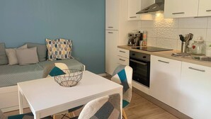 Een knus woongedeelte met kitchenette, een eethoek met tafel en stoelen, en een bank met decoratieve kussens.