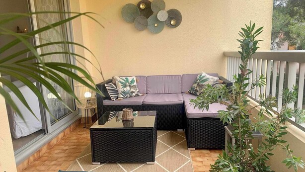 Een balkon met een bank, twee bijzettafels, een salontafel en potplanten.