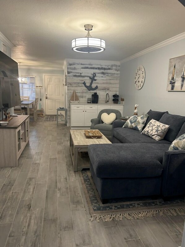 A living room with a dark grey sofa, a wooden coffee table, a white cabinet, and a wall-mounted clock. - VITAMEN SEA AND OCEAN WAVES 3 BDRM RETREAT (Indian Shores)