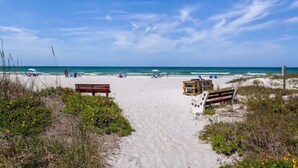 Une plage de sable fin, un ciel dégagé, un banc en bois et une tour de surveillance des sauveteurs.