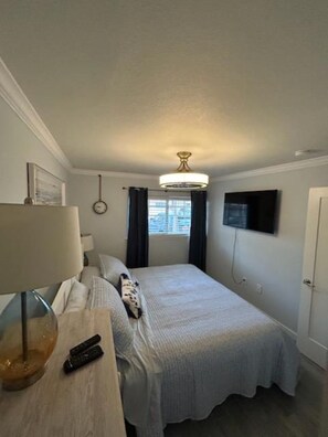 A bedroom with a bed, a lamp, a clock, a TV, and a window. - VITAMEN SEA AND OCEAN WAVES 3 BDRM RETREAT (Indian Shores)