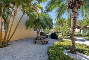 An outdoor patio area with a picnic table, palm trees, and a building with windows. - VITAMEN SEA AND OCEAN WAVES 3 BDRM RETREAT (Indian Shores)