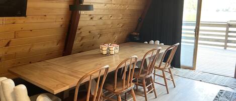 Et træspisebord med stole, en sort vægmonteret lampe og udsigt til det frie gennem et stort vindue.