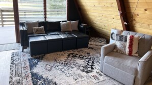 A cozy living room with a black leather sofa, a gray armchair, and a patterned rug. - Holter Lake Water Front Cabin (Wolf Creek)