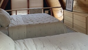A bedroom with a sloped ceiling, wooden walls, and a bed with a white quilted bedspread. - Holter Lake Water Front Cabin (Wolf Creek)