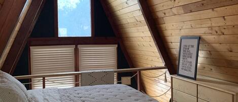 Une chambre avec un plafond en pente, des murs en bois et un lit recouvert d’une courtepointe blanche matelassée.