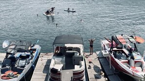 A docked boat with a covered seating area and a small cabin, surrounded by calm water and a forested shoreline. - Holter Lake Water Front Cabin (Wolf Creek)