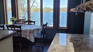 A kitchen with a view of a lake, wooden chairs, a table with a floral tablecloth, and a ceiling fan.
