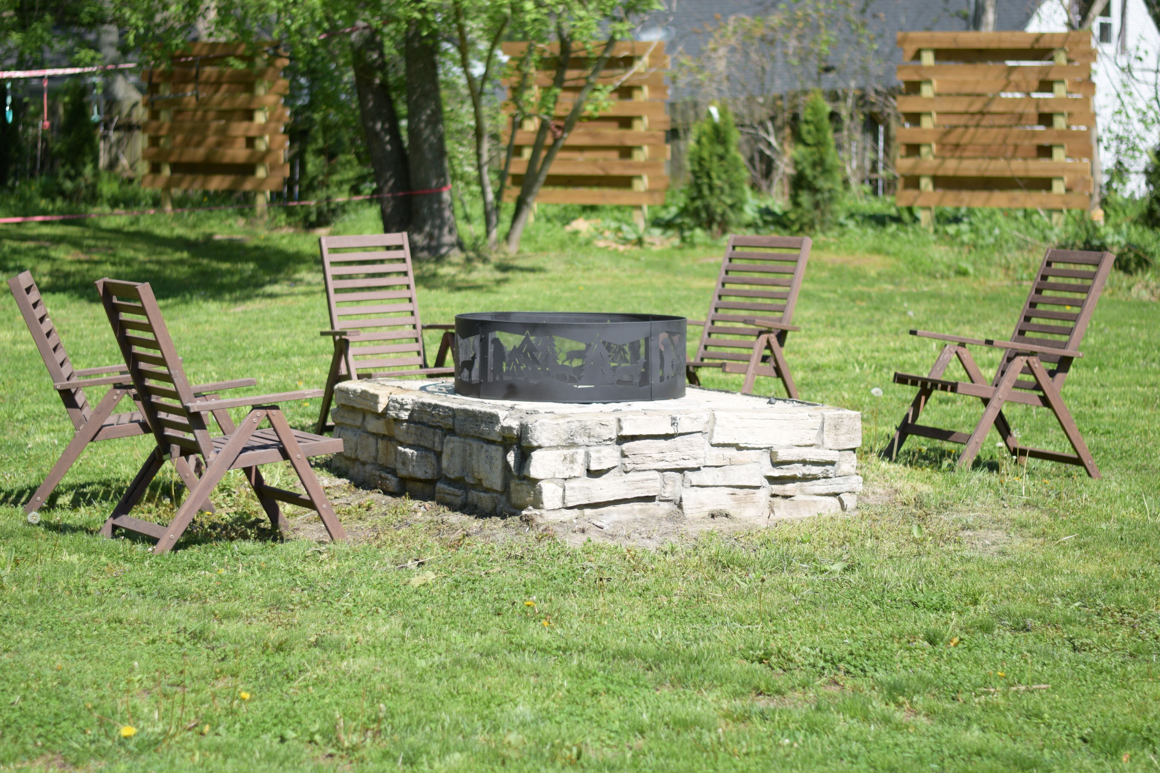 Un hogar de piedra rodeado por cuatro sillas de madera en un espacio al aire libre con césped.