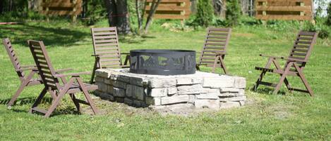 Un hogar de piedra rodeado por cuatro sillas de madera en un espacio al aire libre con césped.