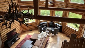 A cozy log cabin interior with a wooden ceiling, large windows, a fireplace, a sofa, and a dining table. - Cozy Log Cabin Near Indiana Dunes & Lake Michigan! (Portage)