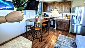 Una cocina moderna con armarios de madera, un refrigerador de acero inoxidable, un horno empotrado y una zona de comedor con taburetes.
