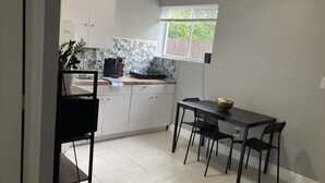 Moderni keittiö, jossa on valkoiset kaapit, työtaso, jossa on kahvinkeitin, ja ikkuna, jossa on sälekaihtimet.