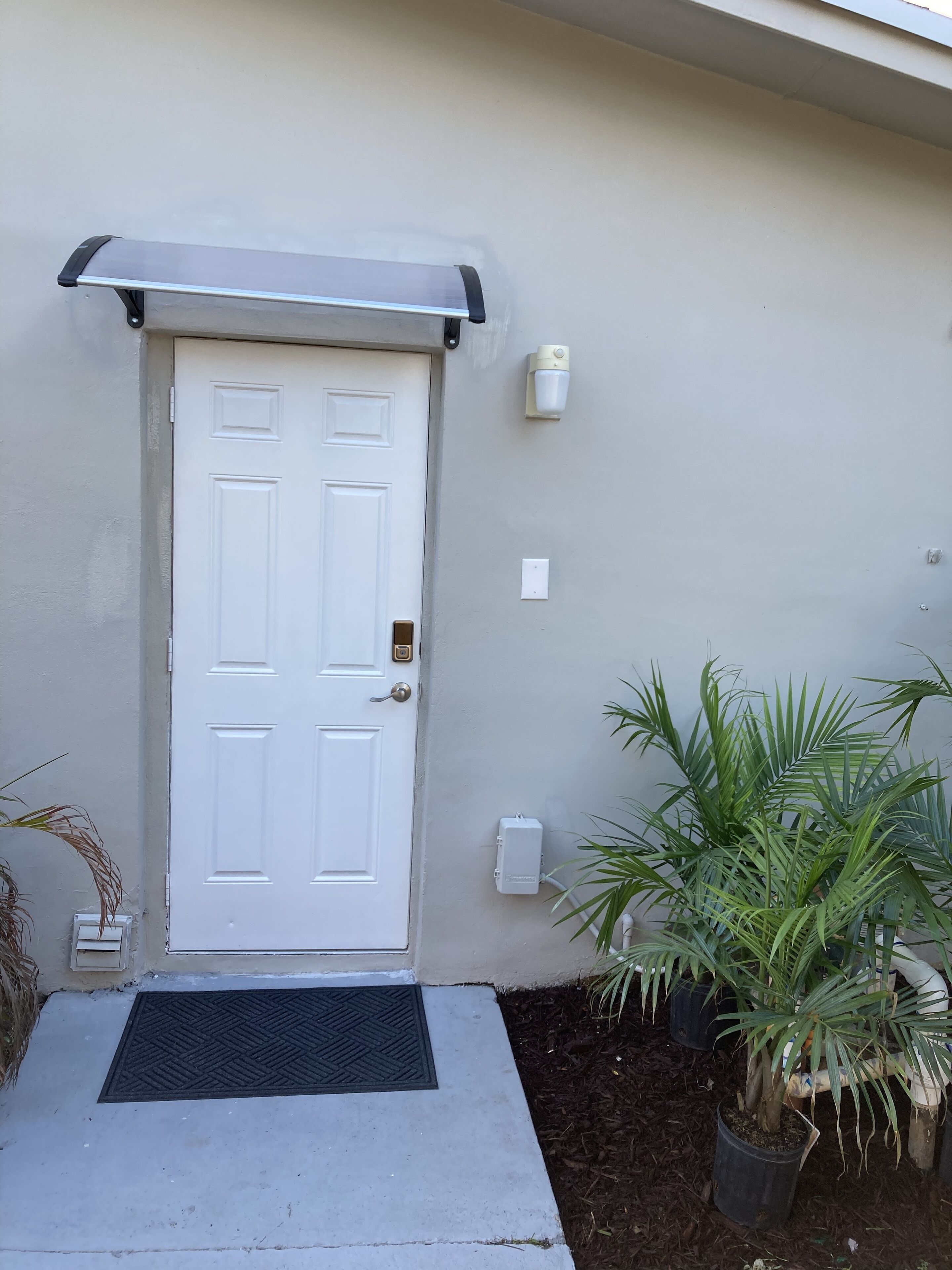 A white door with a metal handle, a small mailbox, and a wall-mounted light fixture.