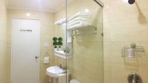 Une salle de bain avec une porte blanche, un lavabo, une douche en verre et des étagères où sont rangées des serviettes et des articles de toilette.