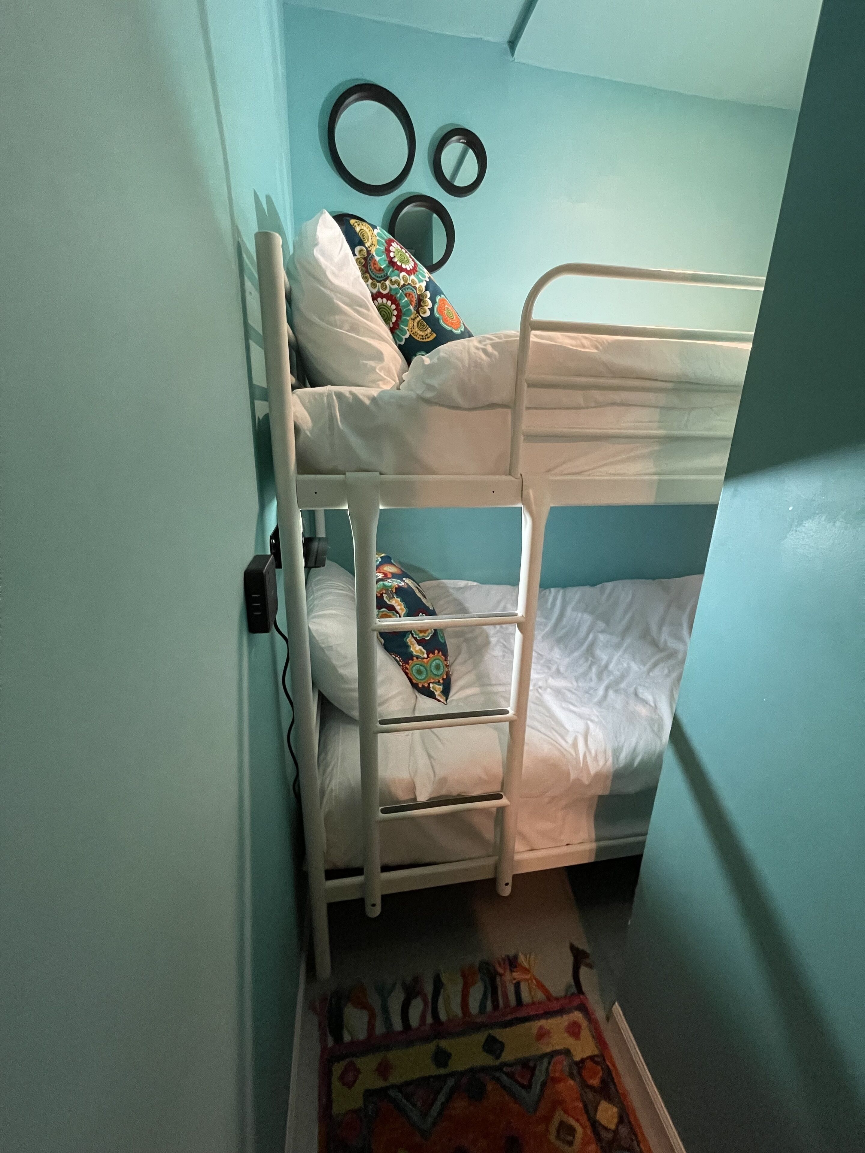 A bunk bed with white bedding and colorful pillows, a small rug, and wall-mounted mirrors.