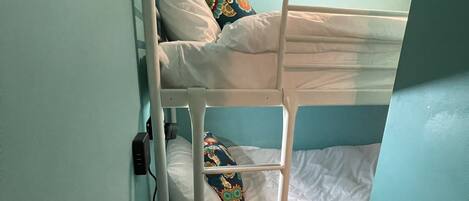 A bunk bed with white bedding and colorful pillows, a small rug, and wall-mounted mirrors.