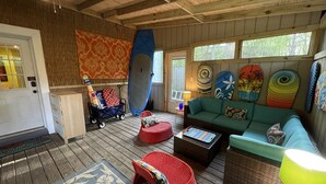 A cozy living room with a wooden floor, a green sofa, a red chair, and a surfboard wall art. - Fun w/Loft! Beach ~Nature Trails ~Grill~ Firepit ~Indiana Dunes National Park  (Gary)