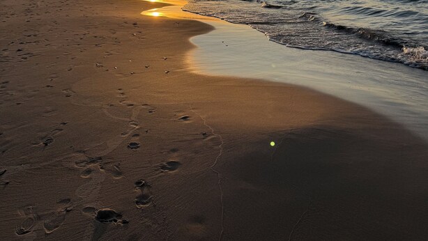 A beach with footprints leading to the water, a boat in the distance, and the sun setting over the horizon. - Fun w/Loft! Beach ~Nature Trails ~Grill~ Firepit ~Indiana Dunes National Park  (Gary)