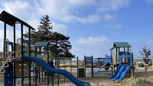A playground with slides and climbing structures, surrounded by sand and sparse vegetation. - Fun w/Loft! Beach ~Nature Trails ~Grill~ Firepit ~Indiana Dunes National Park  (Gary)
