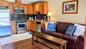 A kitchen with wooden cabinets, stainless steel appliances, and a dining area with a leather sofa and wooden table. - Starboard Cabana - Unit 2 (Chelan)