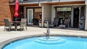 A swimming pool with a metal ladder, surrounded by lounge chairs and a table with a red umbrella. - Starboard Cabana - Unit 2 (Chelan)