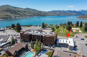 A hotel with a swimming pool, a parking lot, and a view of a lake and mountains.