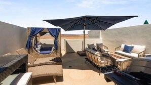 Una terraza en la azotea con mobiliario de mimbre, una silla colgante y una sombrilla.