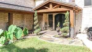 A stone house with a covered porch, a stone fireplace, and a well-maintained garden. - Amazing lakefront home with custom boat dock! (Quinlan)
