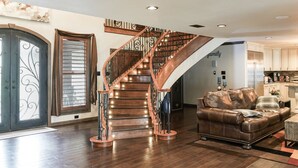 A spacious living room with a wooden staircase, leather sofa, and a kitchen area. - Amazing lakefront home with custom boat dock! (Quinlan)