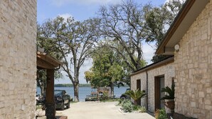 A paved driveway leading to a stone building with a view of a lake. - Amazing lakefront home with custom boat dock! (Quinlan)