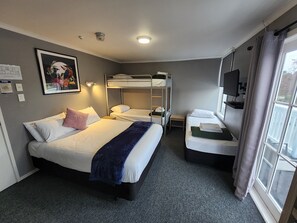 Habitación de hotel con literas, una cama individual, un escritorio, un televisor y una ventana con cortinas.