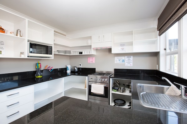 Una cocina moderna con armarios blancos, encimera negra, estufa de acero inoxidable y un lavamanos.