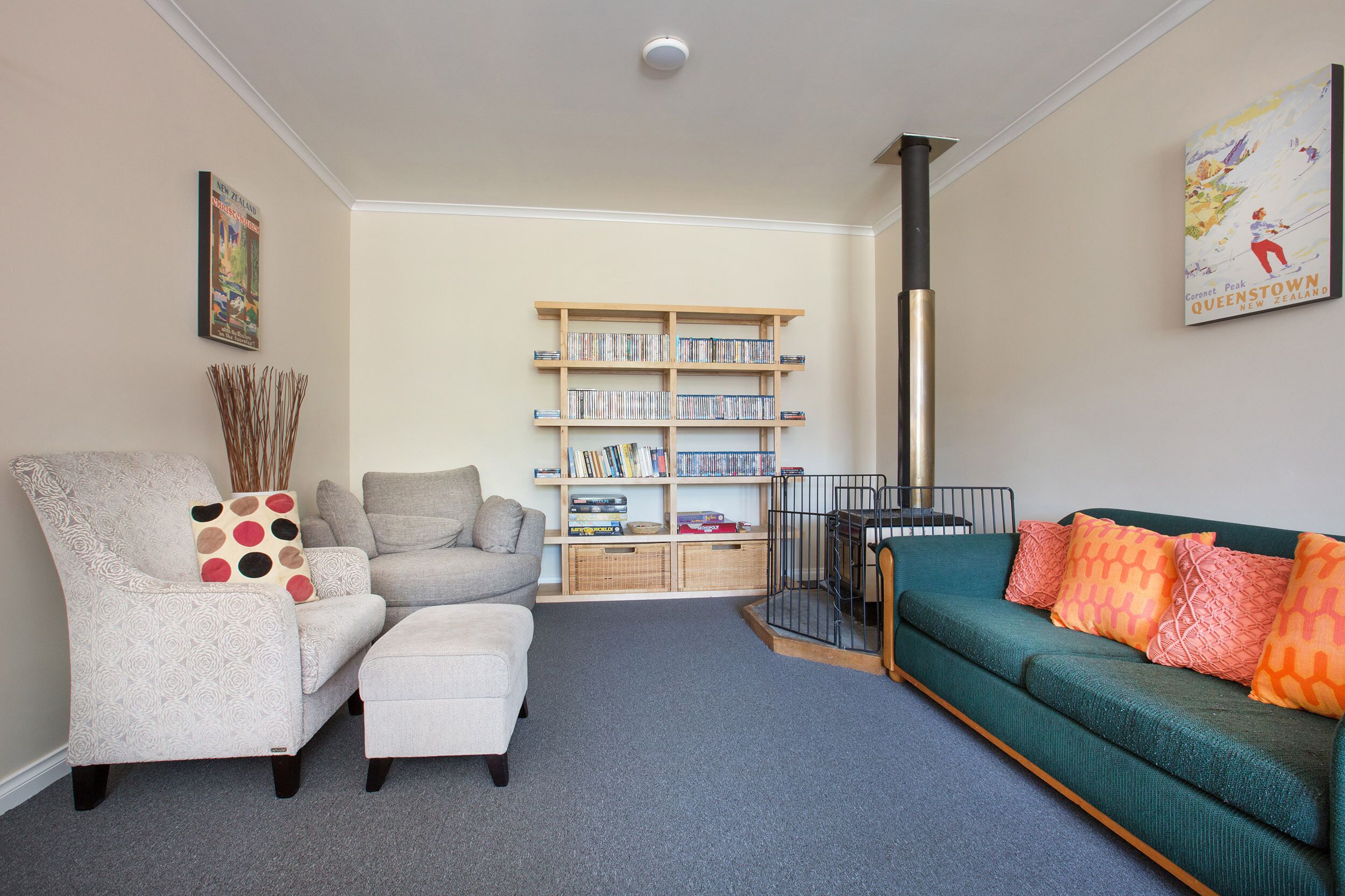 A living room with a grey sofa, a green sofa with orange pillows, a white armchair, and a bookshelf filled with books and decorative items.