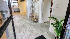 Un pasillo con suelo de madera, un armario blanco, una estantería blanca y una planta en maceta.