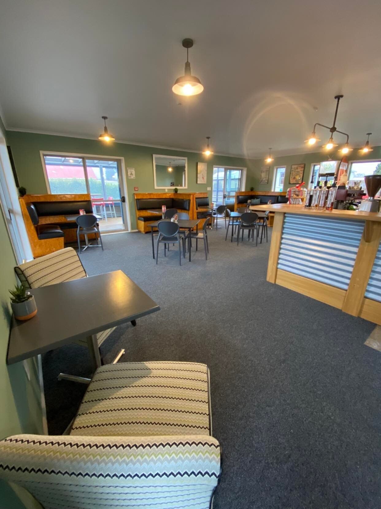A cafe with seating arrangements including booths and tables, a counter with a coffee machine, and a view through a glass door.