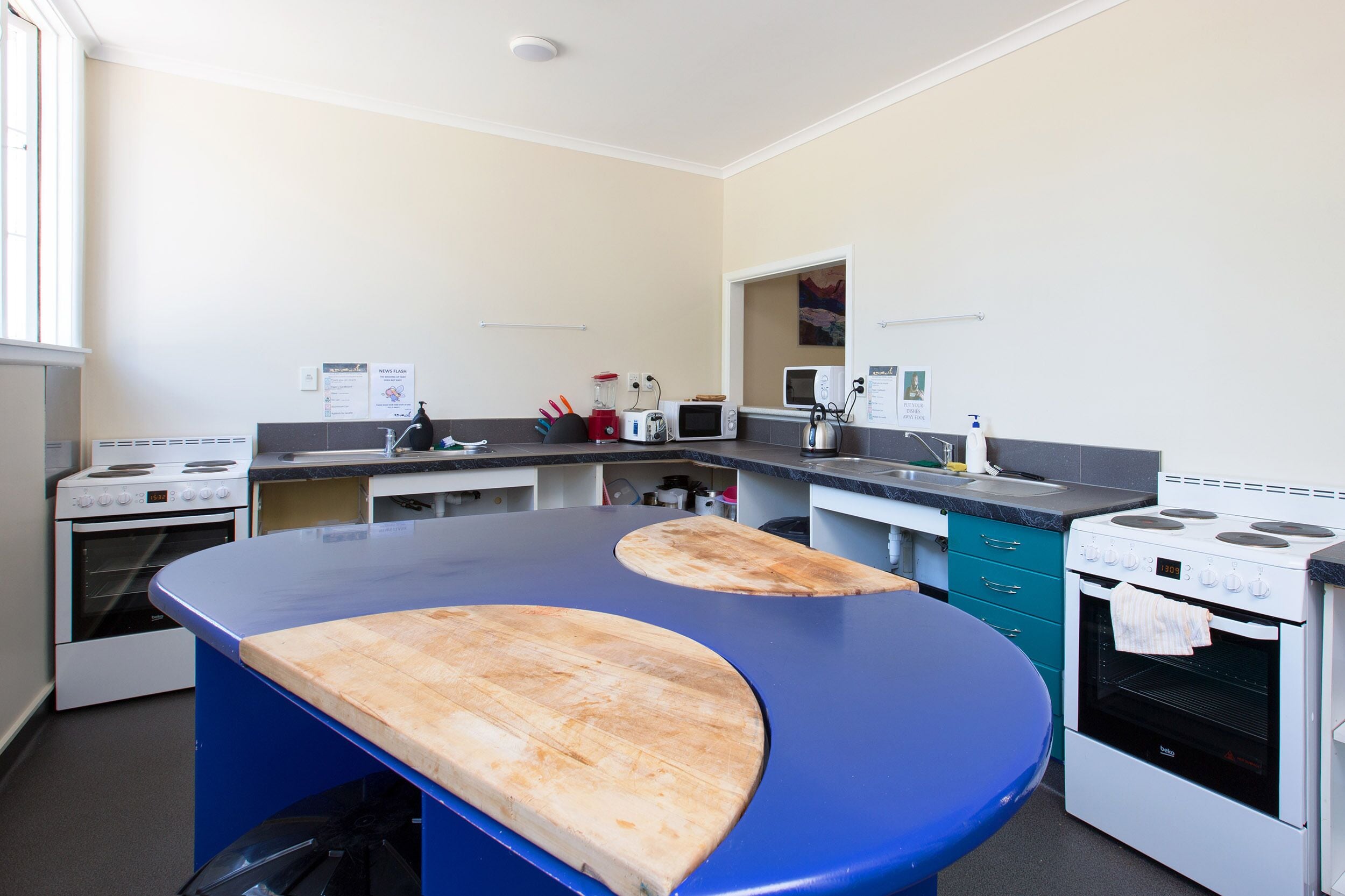A kitchen with a blue countertop, two wooden cutting boards, a microwave, a stove, and a sink.