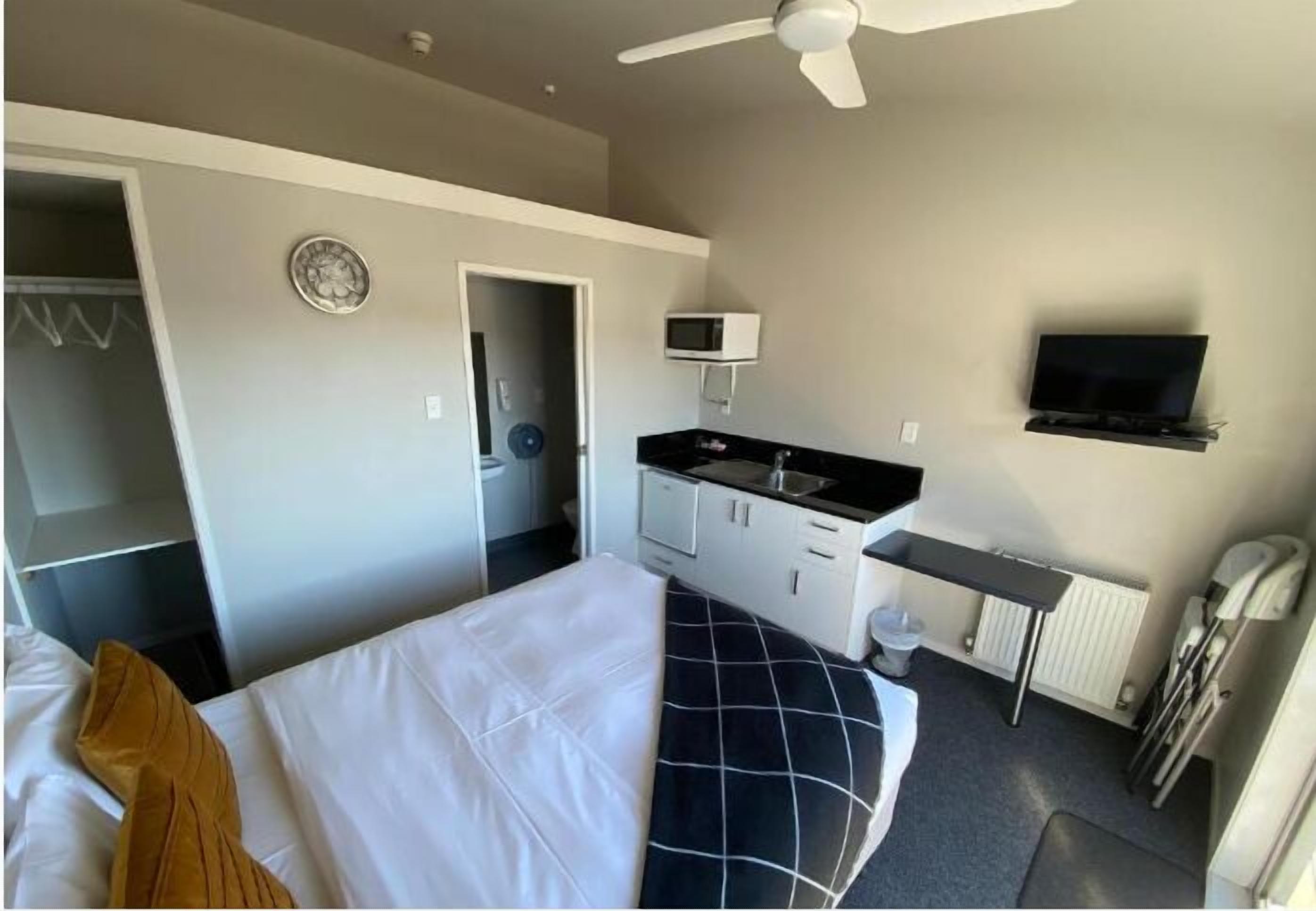 A hotel room with a bed, a desk, a microwave, a TV, and a ceiling fan.
