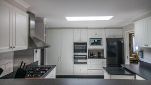 A modern kitchen with white cabinetry, a stainless steel range hood, a built-in oven, a refrigerator, and a coffee maker. - Clarence Homestead - Swim & Relax in the Mountains (Clarence)
