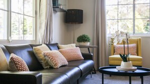 A living room with a dark leather sofa, a round coffee table, and a yellow armchair. There are potted plants on a side table and a large window providing natural light. - Clarence Homestead - Swim & Relax in the Mountains (Clarence)
