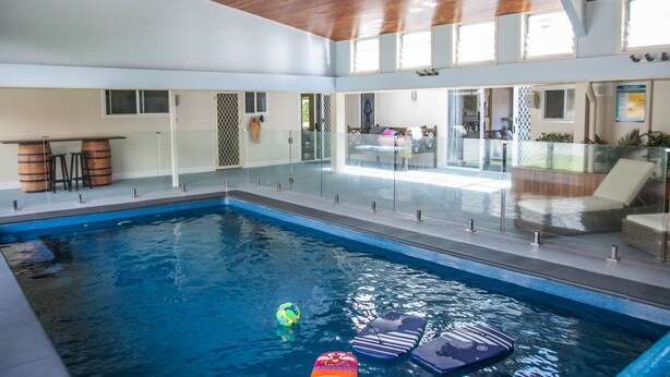 An indoor swimming pool with clear glass walls, wooden ceiling, and a seating area with loungers. - Clarence Homestead - Swim & Relax in the Mountains (Clarence)