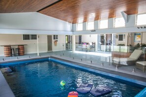 Une piscine intérieure avec des parois en verre transparent, un plafond en bois et un espace détente équipé de chaises longues.