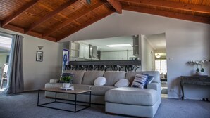 A spacious living room with a high ceiling, a ceiling fan, a sofa set, a coffee table, and a kitchen area visible through an open doorway. - Clarence Homestead - Swim & Relax in the Mountains (Clarence)